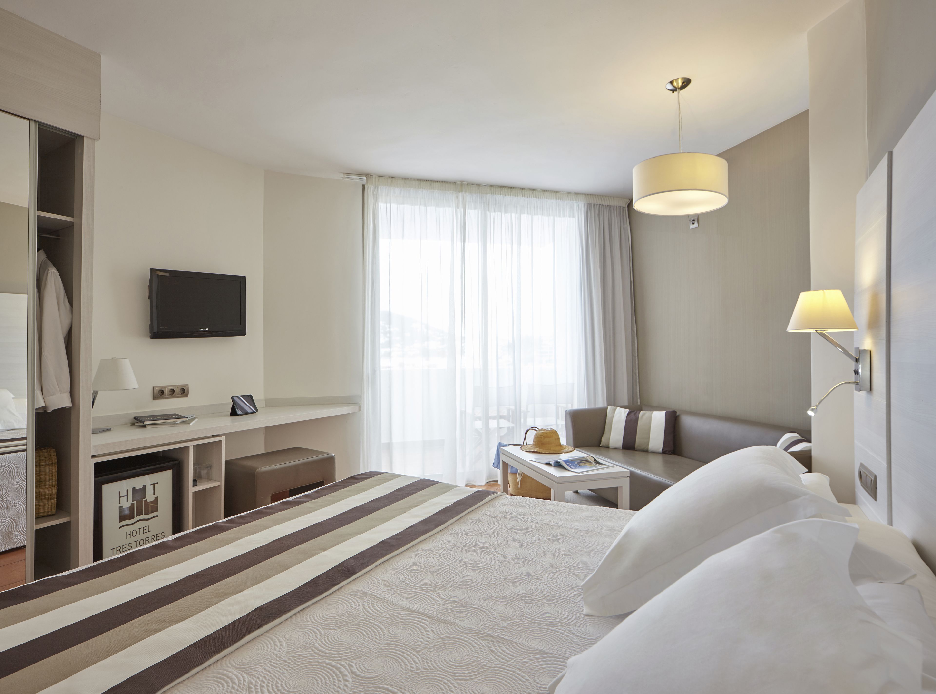 Ein Hotelzimmer mit Bett, Schreibtisch, Stuhl, Fernseher und einem Fenster mit Vorhängen.