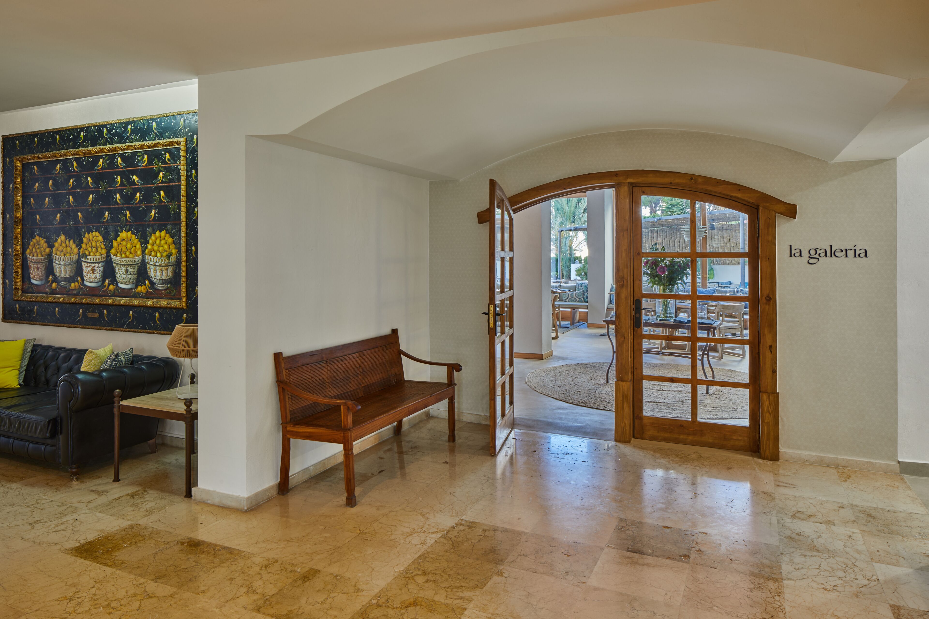 Un hall d’entrée spacieux avec un banc en bois, une grande peinture murale et une porte portant l’inscription « la galerie ».