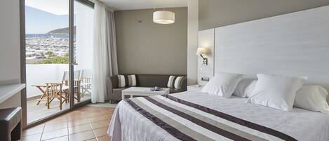 A hotel room with a large bed, a balcony with a view, a small table, and a sofa.