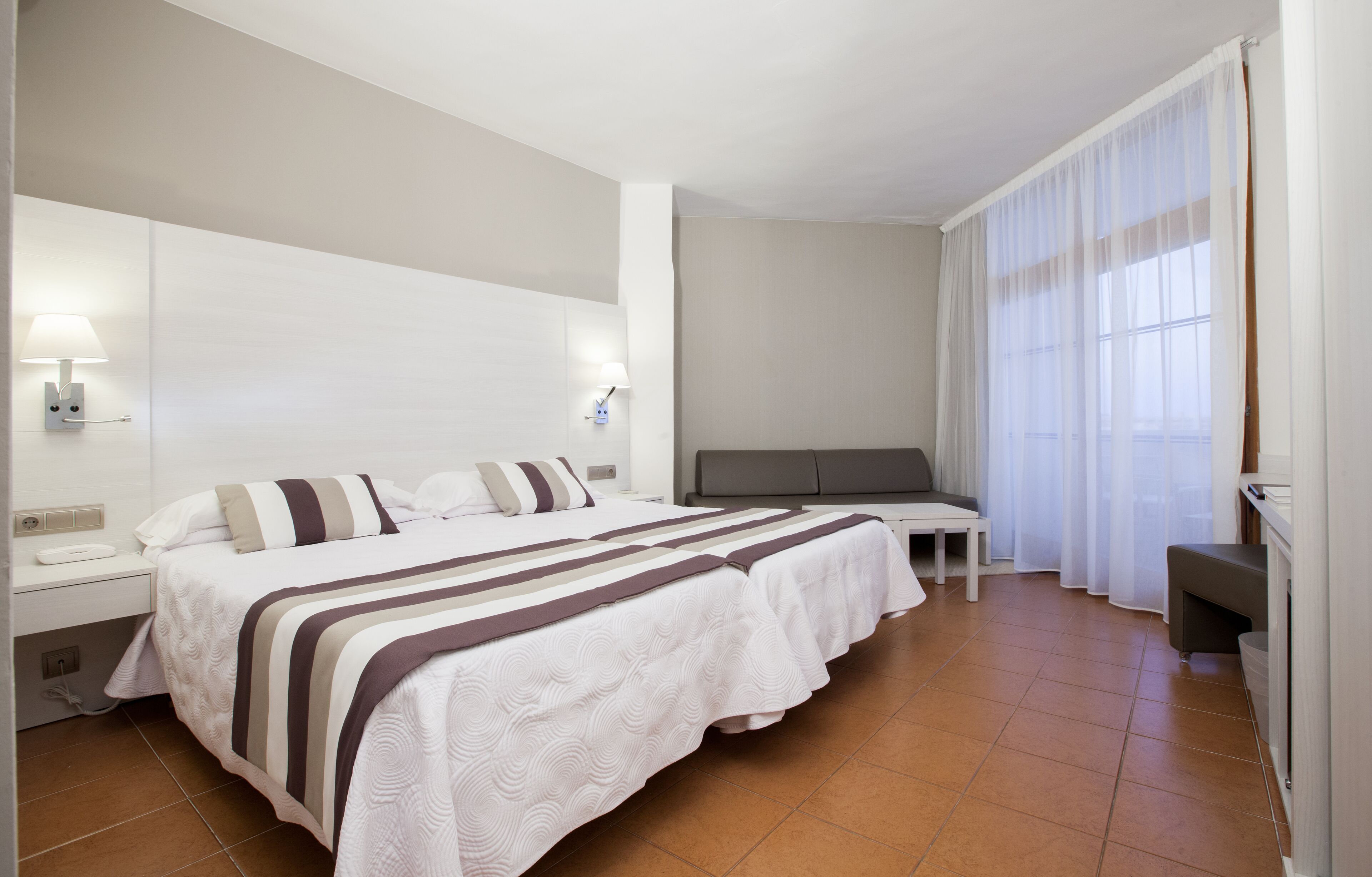 A hotel room with a large bed, bedside tables, a desk, and a chair.