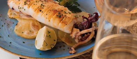 Un plato de pescado con limón y hierbas, una copa de vino blanco y un posavasos tejido.