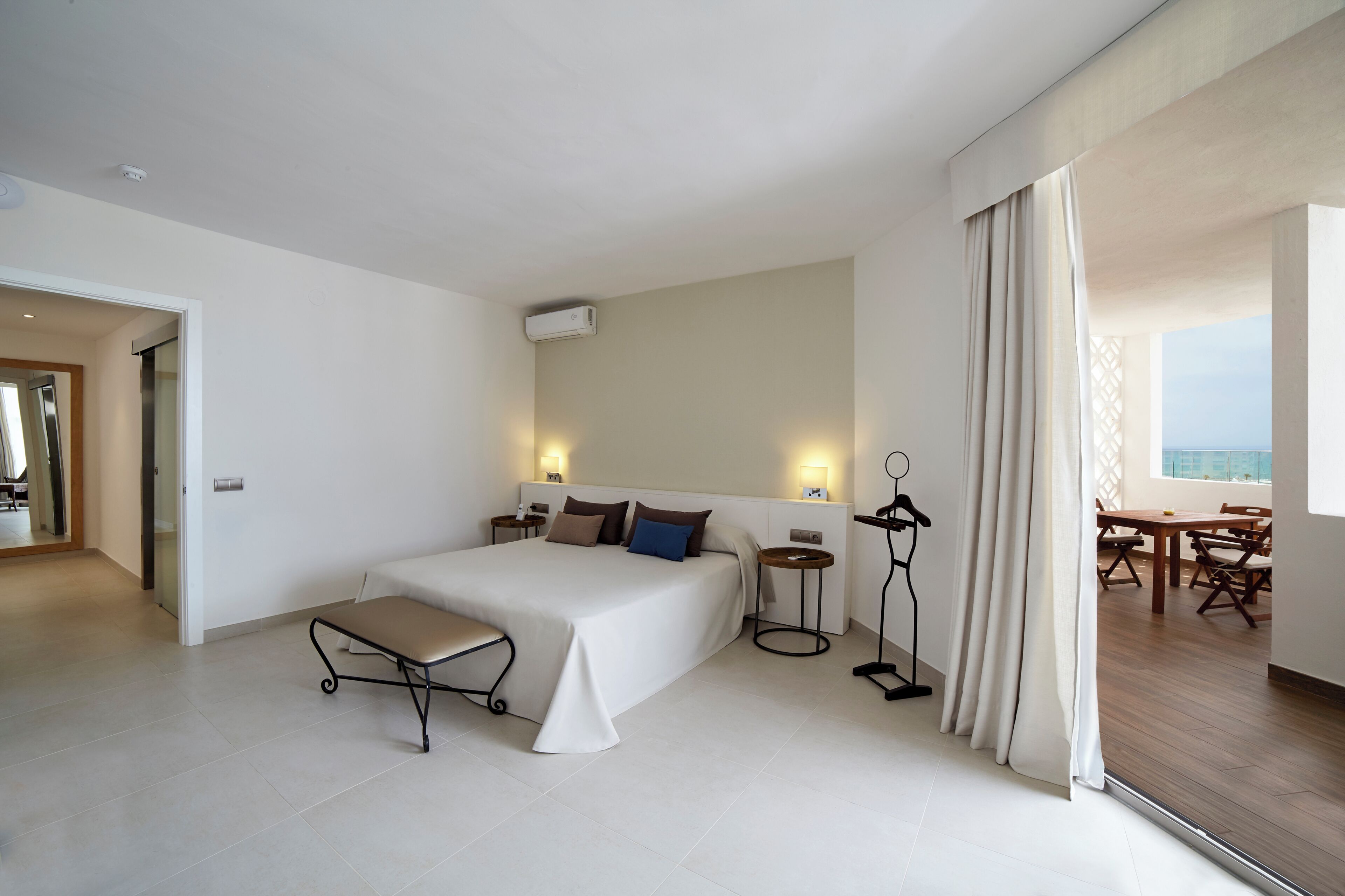A hotel room with a bed, bedside tables, a desk, and a view of the sea.
