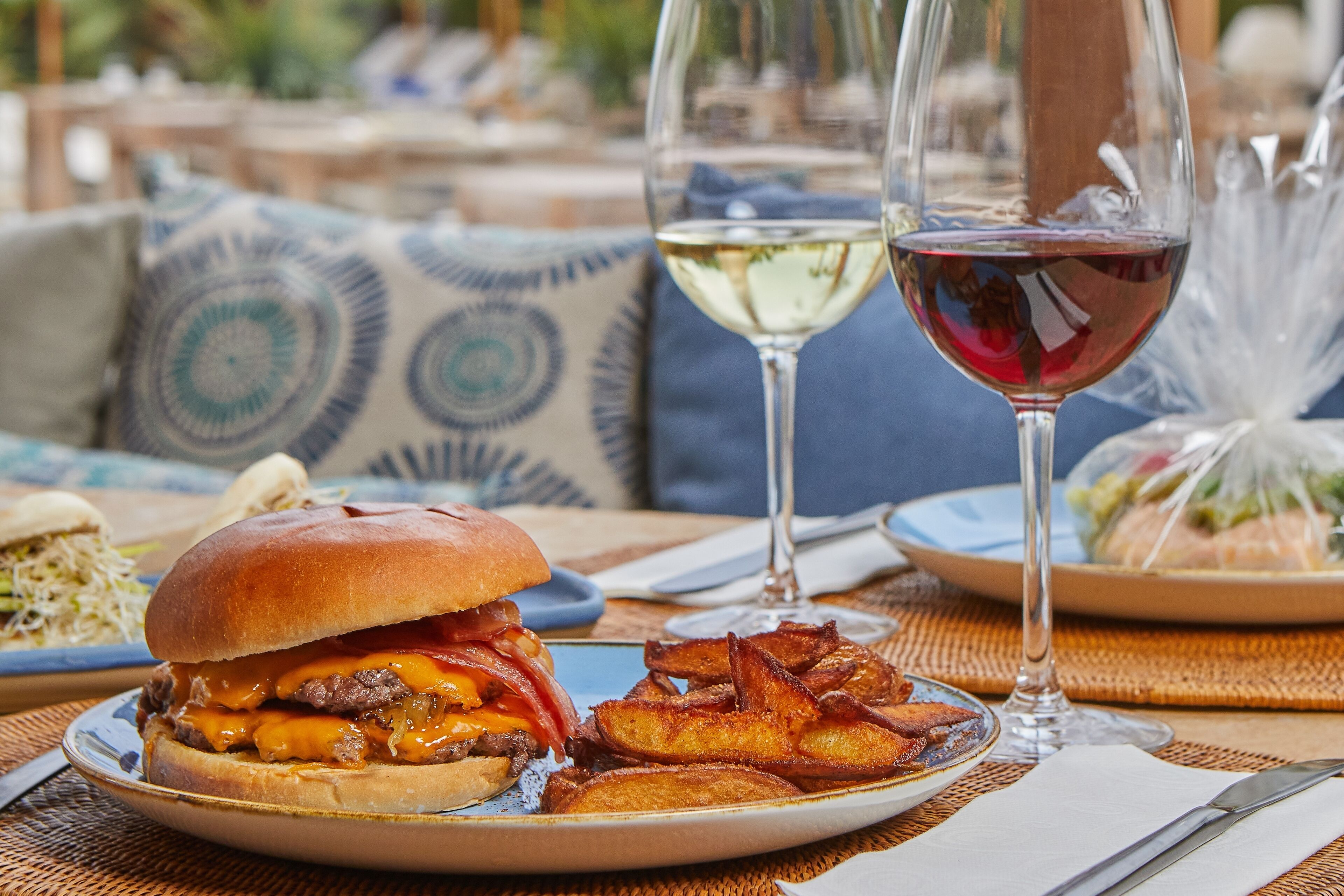 Un plato con una hamburguesa, papas fritas y una copa de vino blanco sobre una mesa.