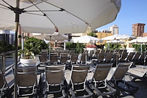 Terrassensitzgelegenheiten mit Sonnenschirmen, in Reihen angeordnet, mit Blick auf eine Skyline aus Gebäuden und Palmen.