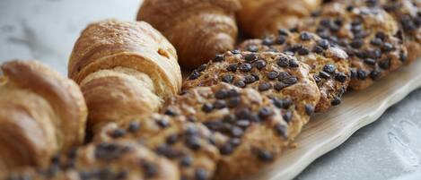 A variety of baked goods, including croissants and a chocolate chip cookie bread, displayed on a wooden board.