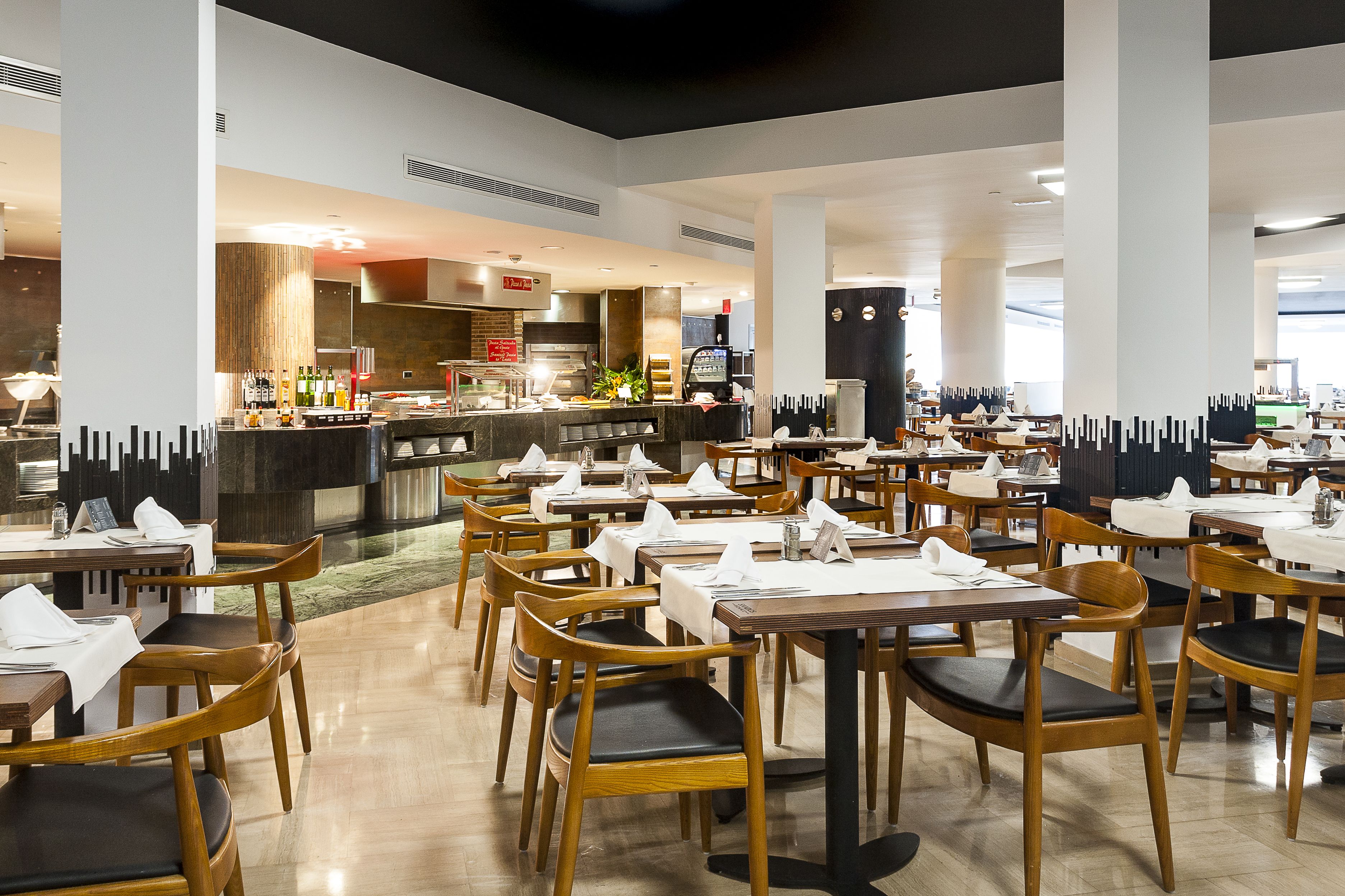 A spacious restaurant with multiple tables and chairs, a visible kitchen area, and a modern interior design.
