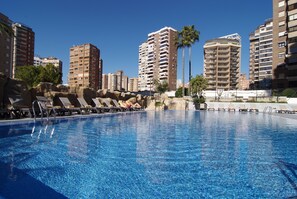 A swimming pool with lounge chairs and palm trees, surrounded by high-rise buildings.