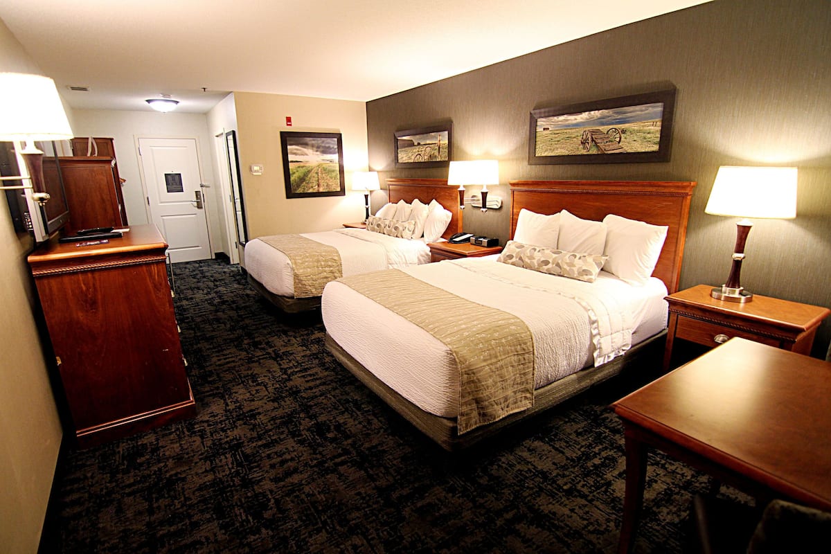 A hotel room with two beds, a desk, a chair, a dresser, and a door.