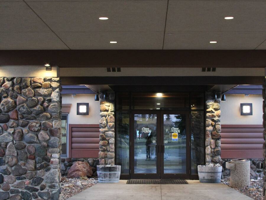 Entrada de hotel con fachada de piedra, puerta de cristal y un sendero de hormigón que lleva a la entrada.