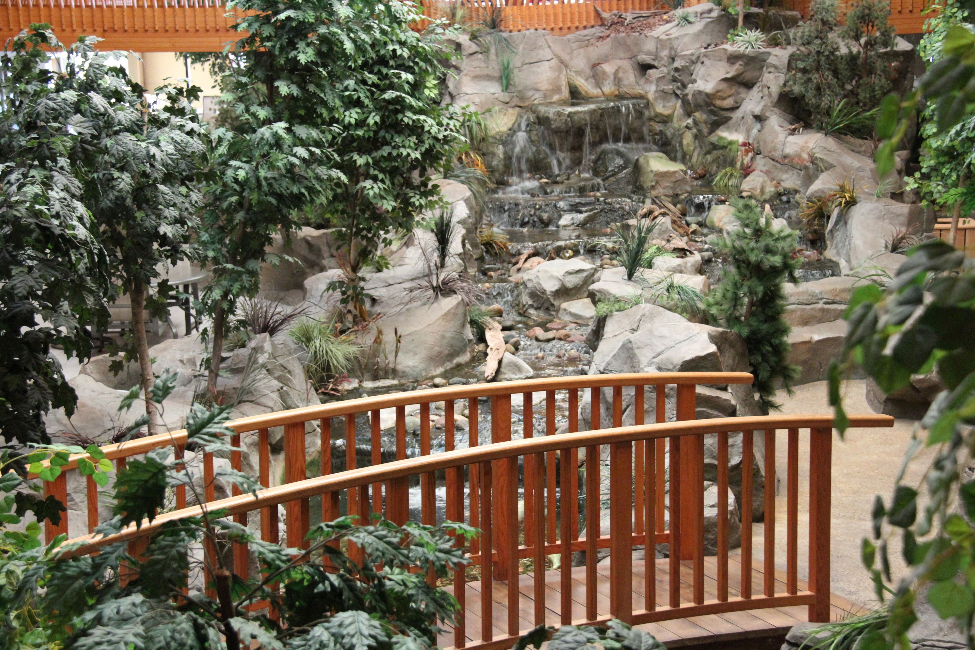 A wooden bridge over a rocky garden with a waterfall.
