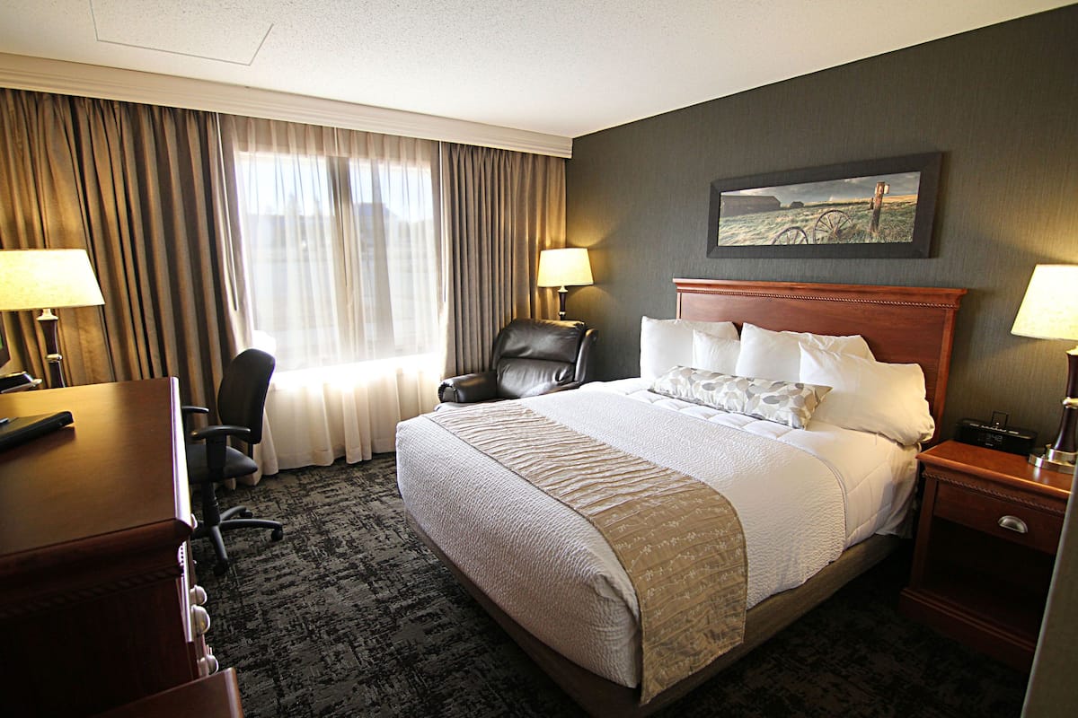 A hotel room with a large bed, two bedside tables, a desk, a chair, and a window with curtains.