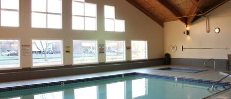 Une piscine intérieure dotée de grandes baies vitrées, de poutres en bois et d’un revêtement de sol carrelé.