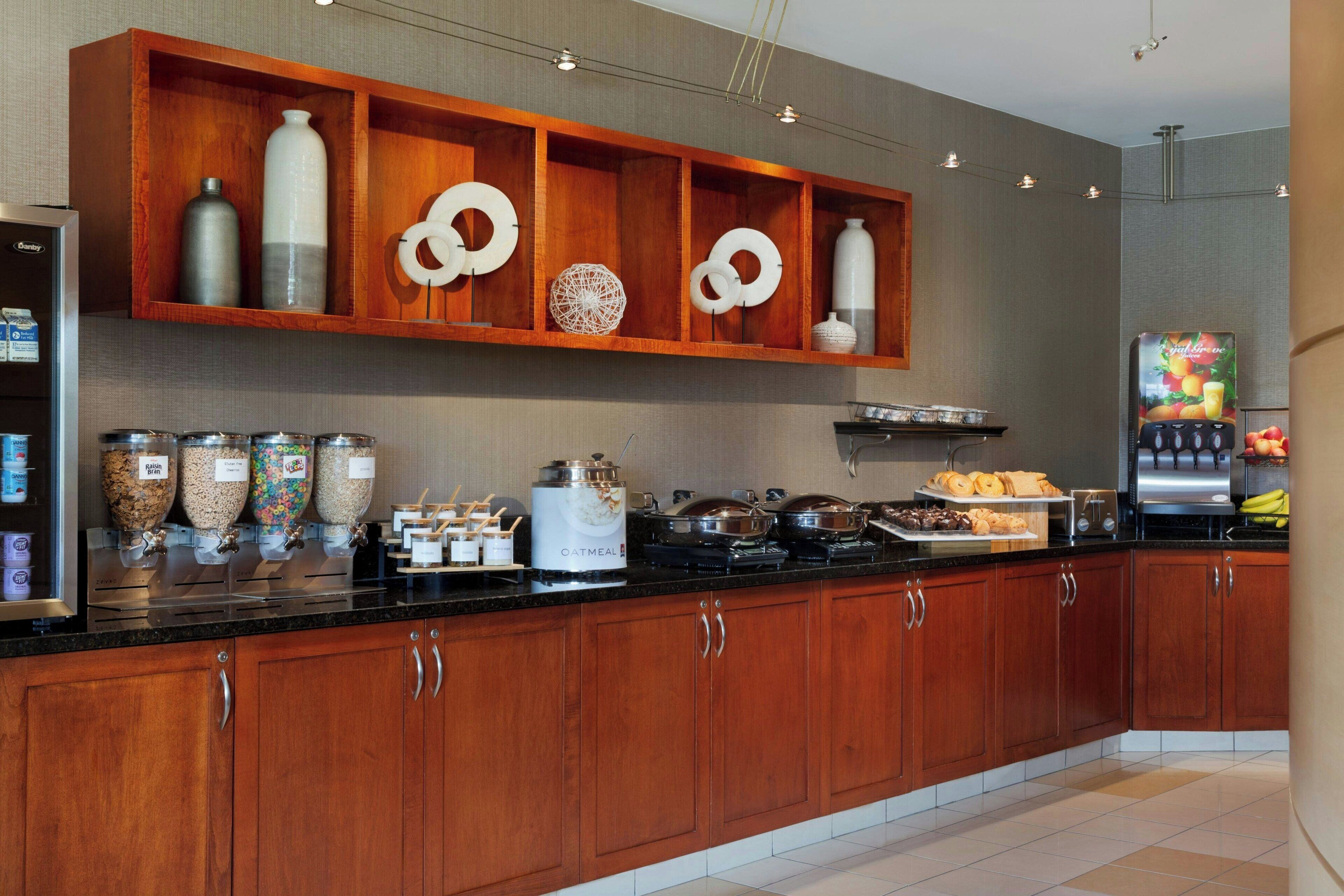 A modern kitchen with wooden cabinets, a black countertop, and various food items and appliances.