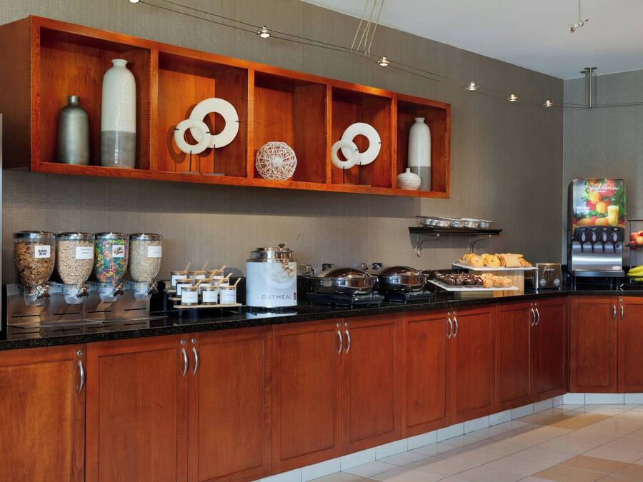 Cocina moderna con armarios de madera, encimera negra y diferentes alimentos y electrodomésticos.