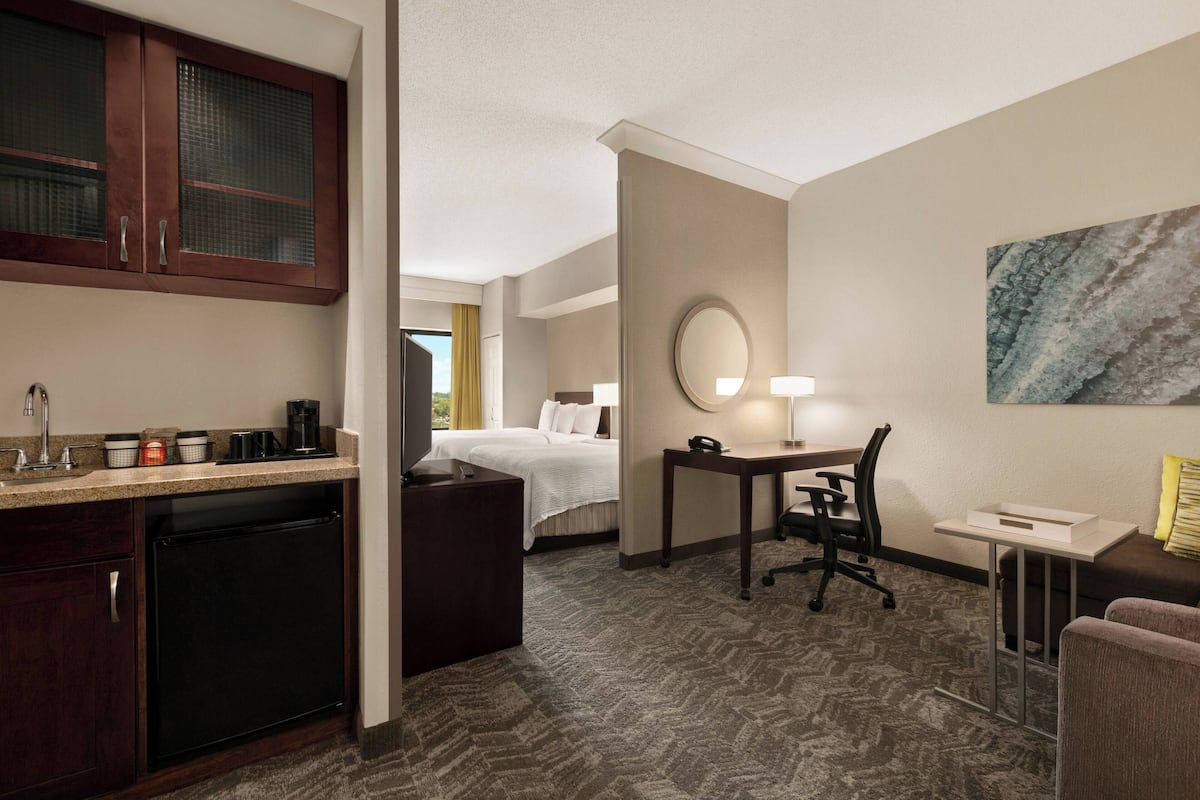 A hotel room with a kitchenette, a bed, a desk with a chair, a small table, and a large mirror.