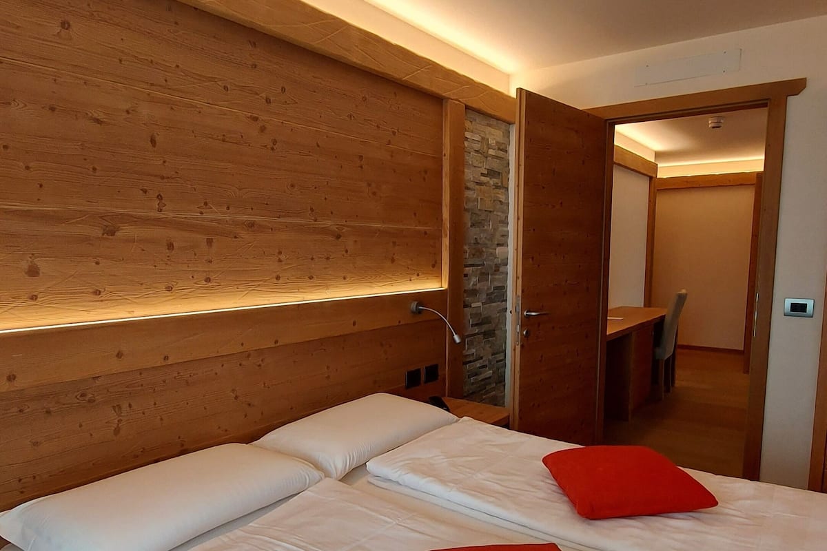 Een slaapkamer met een houten hoofdbord, een bed met witte beddengoed en rode kussens, en een accentmuur van steen.