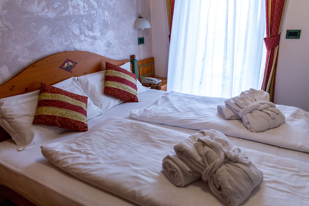 Een hotelkamer met twee bedden, elk voorzien van witte lakens en decoratieve kussens. Er liggen handdoeken op de bedden en een lamp op het nachtkastje.