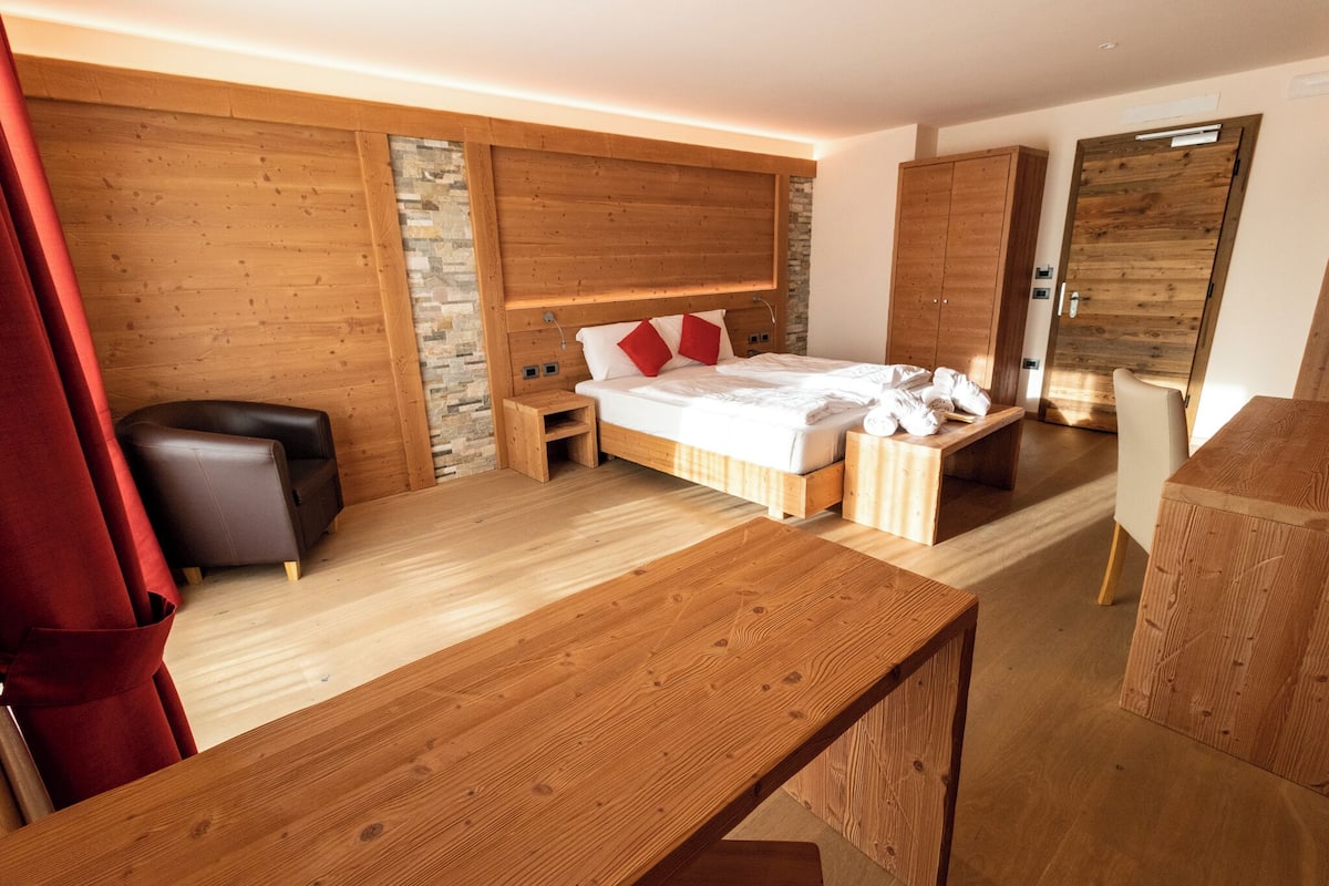 Een moderne slaapkamer met een houten hoofdbord, een groot bed, een nachtkastje van hout, een houten bankje, een rood gordijn en een houten garderobe.