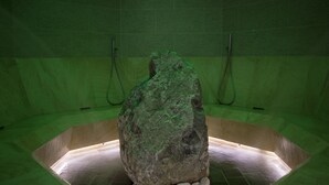 Een stenen badkuip met een groen verlicht interieur, omgeven door een betegelde vloer en muren.