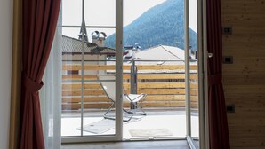 Een kamer met een schuifglazen deur die uitkomt op een balkon met uitzicht op een berg en traditionele gebouwen.