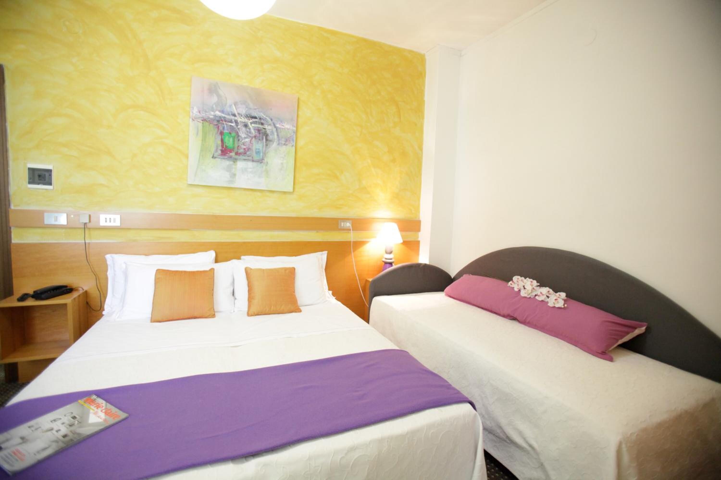 Camera d'albergo con due letti, un comodino con telefono, una lampada e un quadro appeso al muro.
