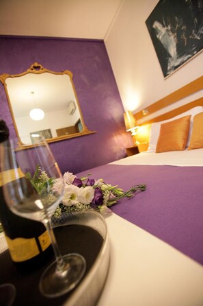 A hotel room with a purple wall, a bed with white and brown bedding, a nightstand with a lamp, and a mirror on the wall. - Art Hotel (Mirano)