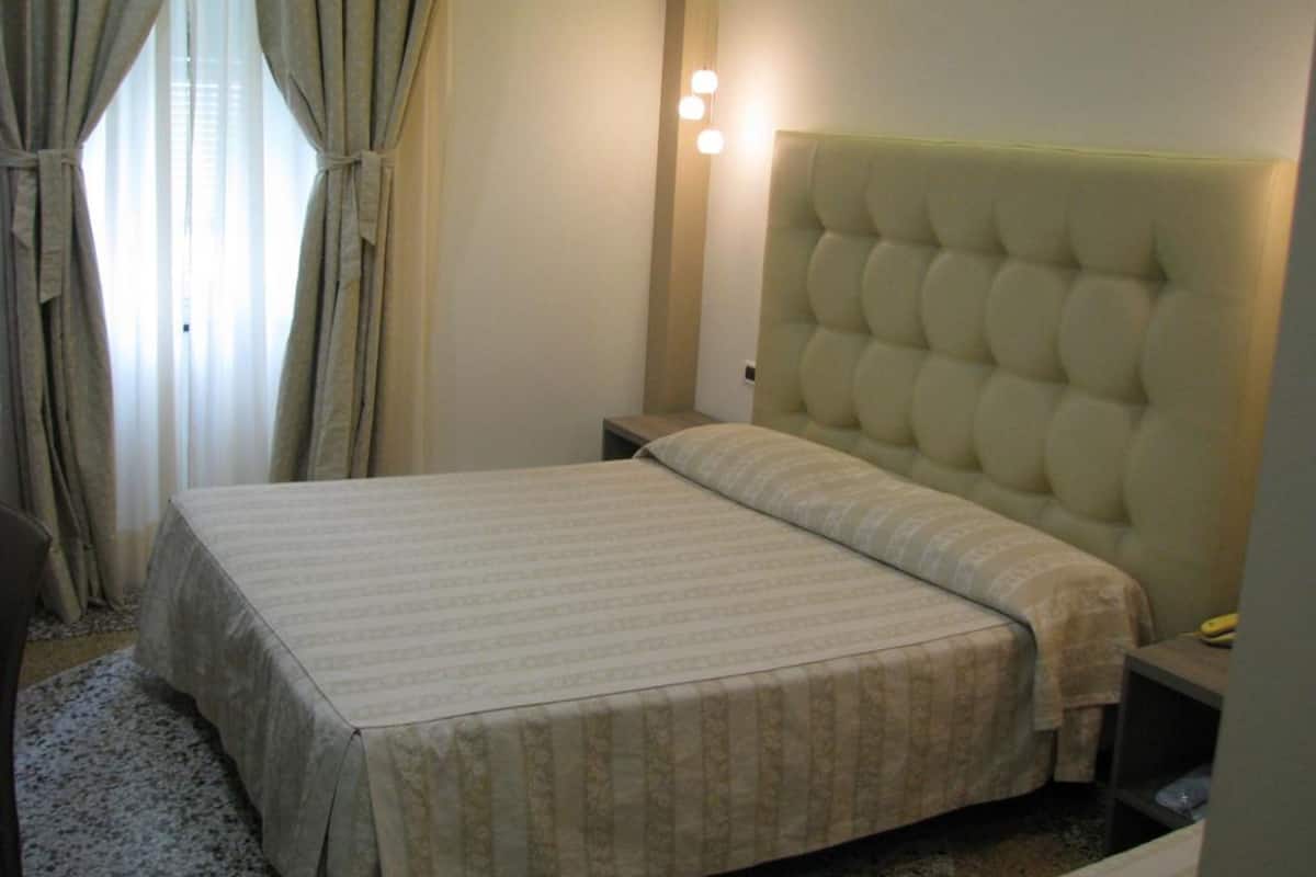 Una habitación de hotel con una cama, una mesita de noche, una lámpara y cortinas.