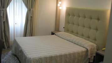 A hotel room with a bed, a nightstand, a lamp, and curtains.