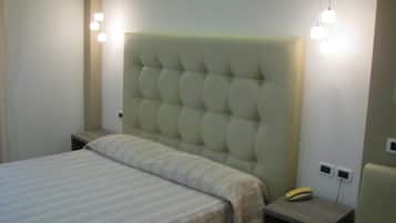 Un dormitorio con cabecera capitonada, cama con colcha a rayas, mesita de noche con lámpara y velador con teléfono.