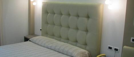 A bedroom with a tufted headboard, a bed with a striped bedspread, a bedside table with a lamp, and a nightstand with a telephone.