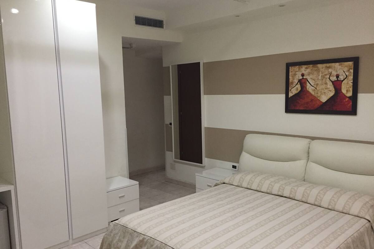 Un dormitorio con cama, armario, mesita de noche y un cuadro en la pared.