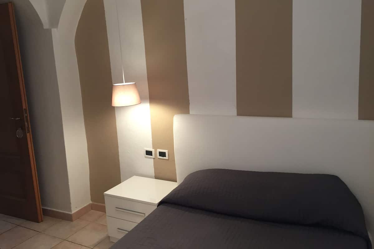 Un dormitorio con cama, mesita de noche, lámpara y puerta.