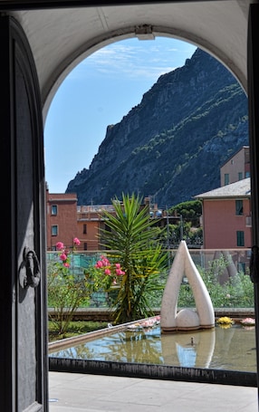 A view through an arched window of a building with a mountain in the background, a fountain, and some greenery.