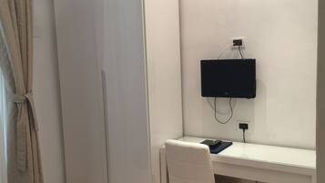 Un dormitorio con cama, un escritorio con silla, un armario y un televisor montado en la pared.