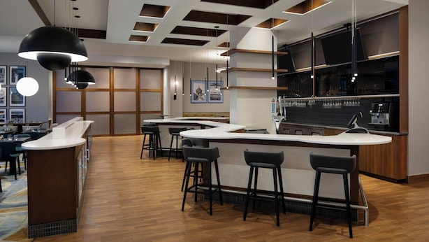A modern bar area with a curved counter, multiple stools, and pendant lighting. - Courtyard by Marriott Montreal Airport (Montreal)