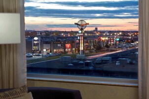 A view from a window overlooking a cityscape at dusk, featuring a prominent cinema sign, a parking lot, and a street with moving vehicles.