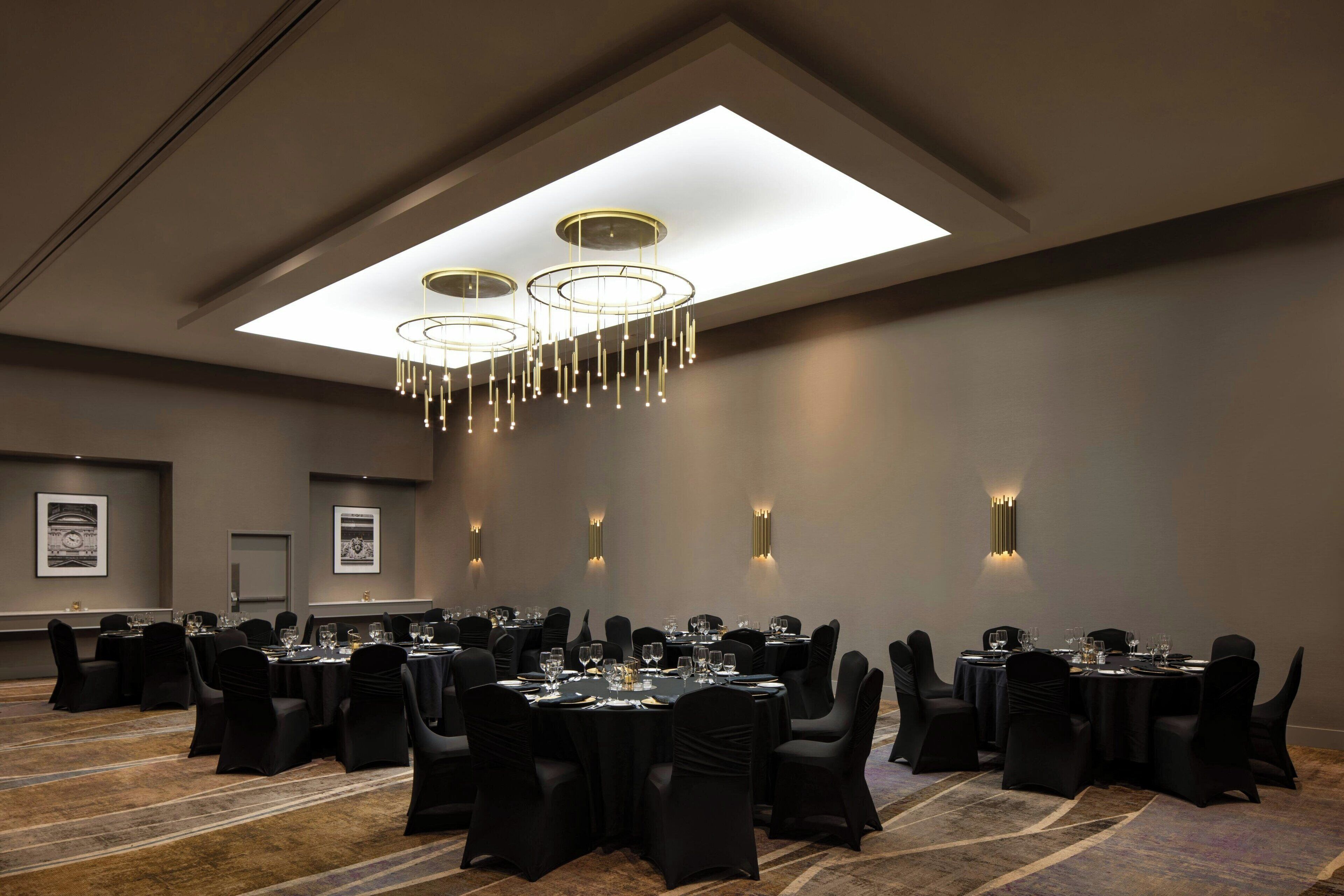 Une salle de conférence avec des tables rondes, des chaises noires et un lustre moderne.