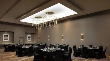 Une salle de conférence avec des tables rondes, des chaises noires et un lustre moderne.