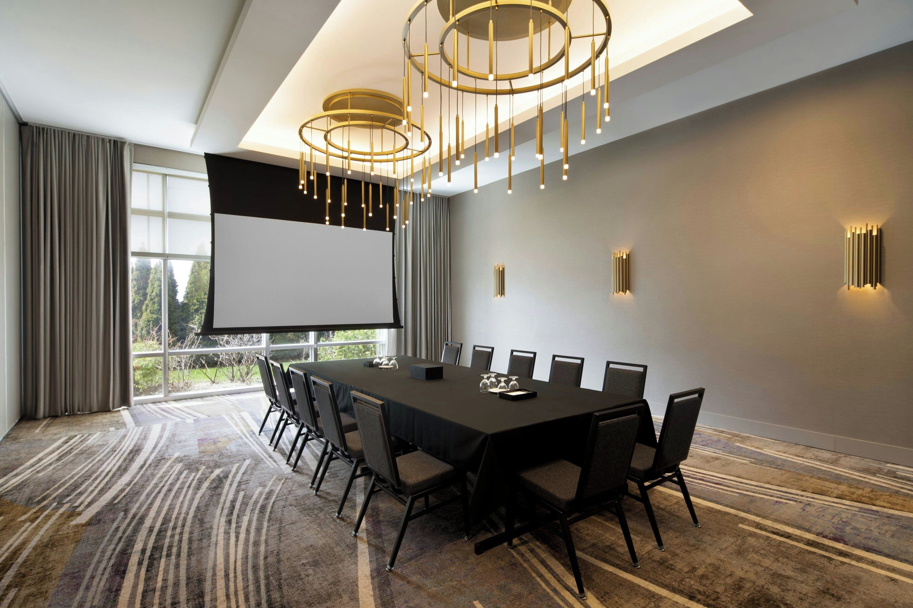 A conference room with a long table, chairs, a projector screen, and a large window with curtains.