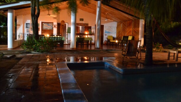 Un espacio exterior techado con piscina, asientos y bar.