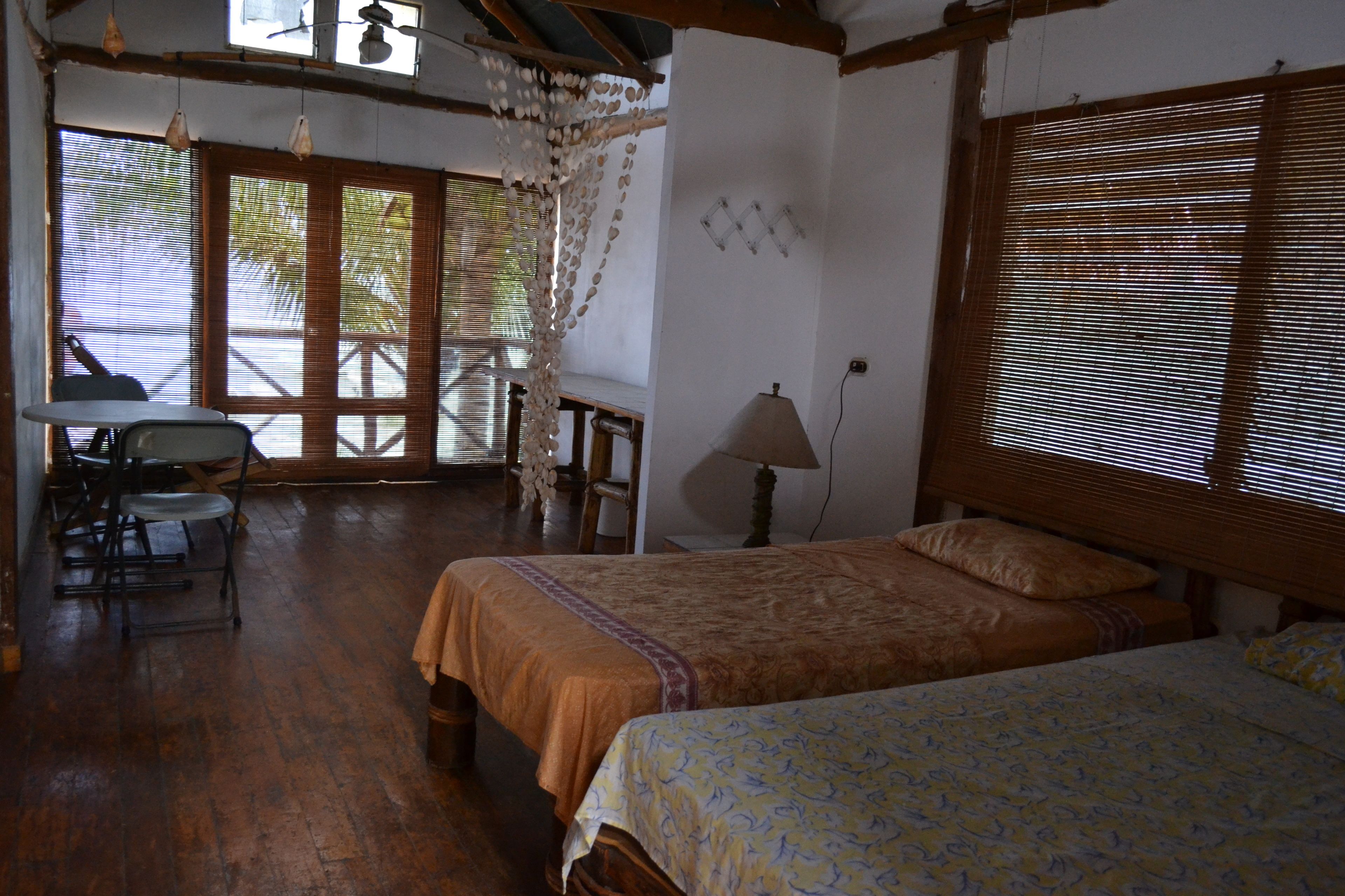 Una habitación con dos camas, una mesa, sillas, una lámpara y vistas al exterior.