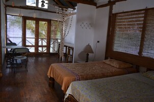 Una habitación con dos camas, una mesa, sillas, una lámpara y vistas al exterior.