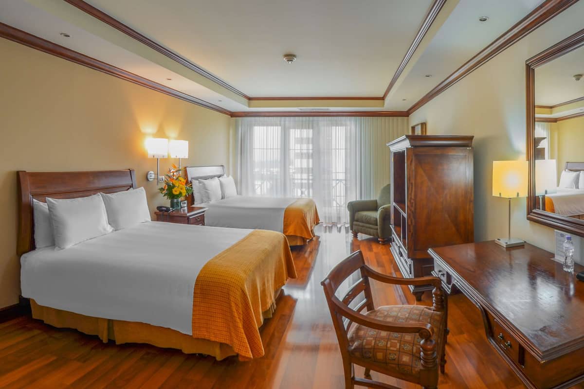 Habitación de hotel con dos camas, un escritorio, una silla, un armario y un espejo grande.
