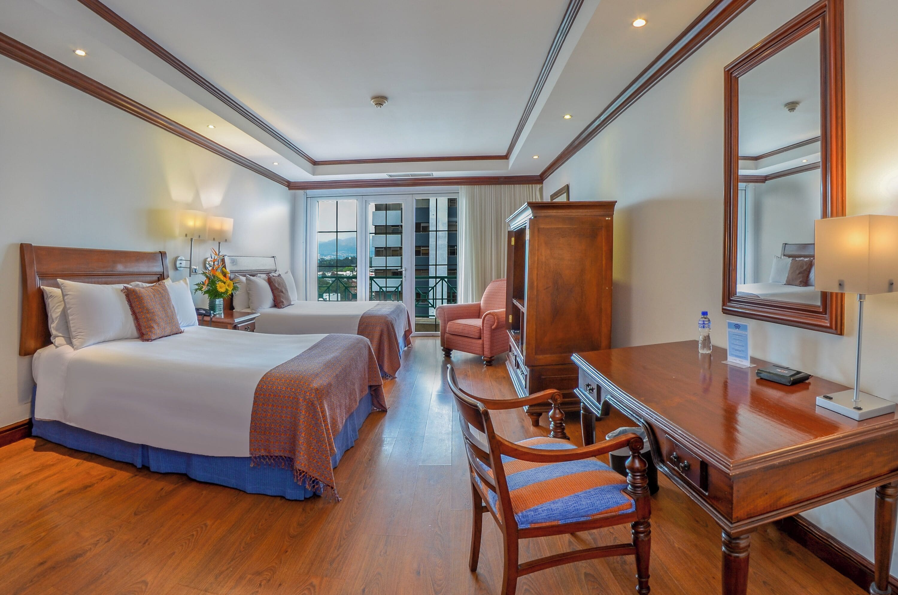 A hotel room with a large bed, a desk, a chair, and a mirror.