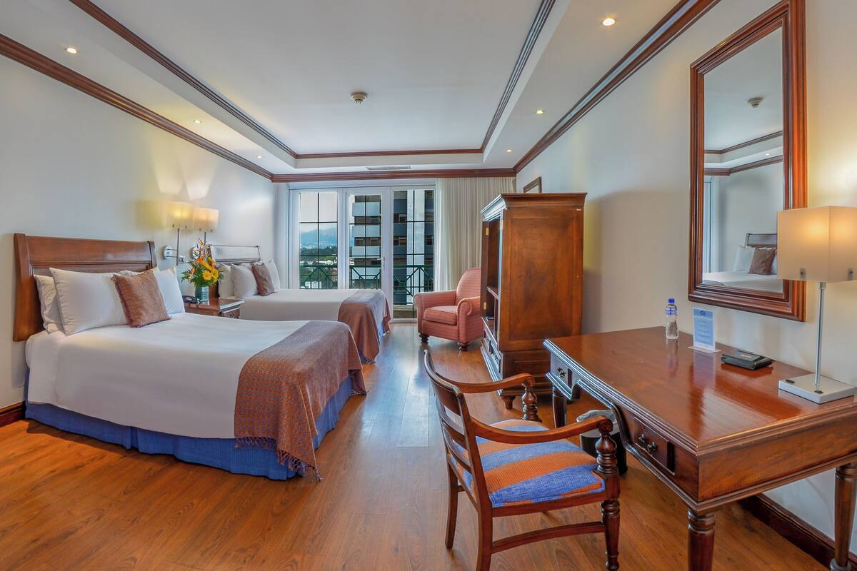 Una habitación de hotel con una cama grande, un escritorio, una silla y un espejo.