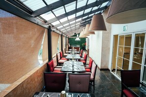 A restaurant with a covered outdoor seating area, red upholstered chairs, and a green wall in the background. - Hotel Casa Veranda (Guatemala City)