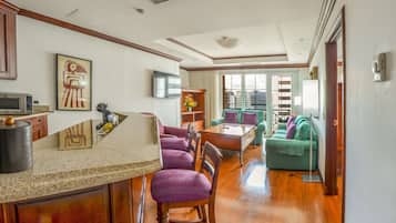 A modern hotel room with a kitchen area, a dining table, and a green sofa.