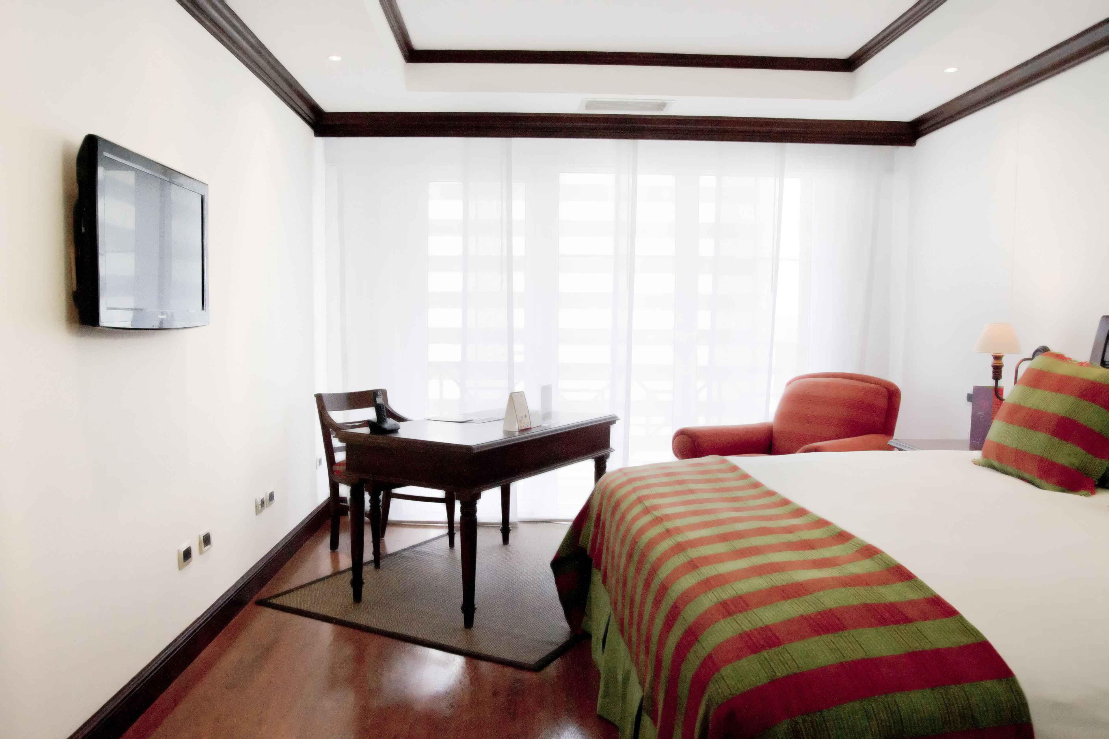 A hotel room with a bed, a desk, a chair, a television, and a window with curtains.