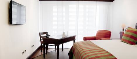 Une chambre d’hôtel équipée d’un lit, d’un bureau, d’une chaise, d’une télévision et d’une fenêtre avec des rideaux.