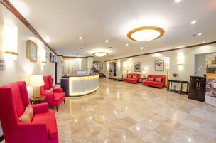 Un vestíbulo amplio con una recepción, zona de estar con asientos rojos e iluminación cuidada.